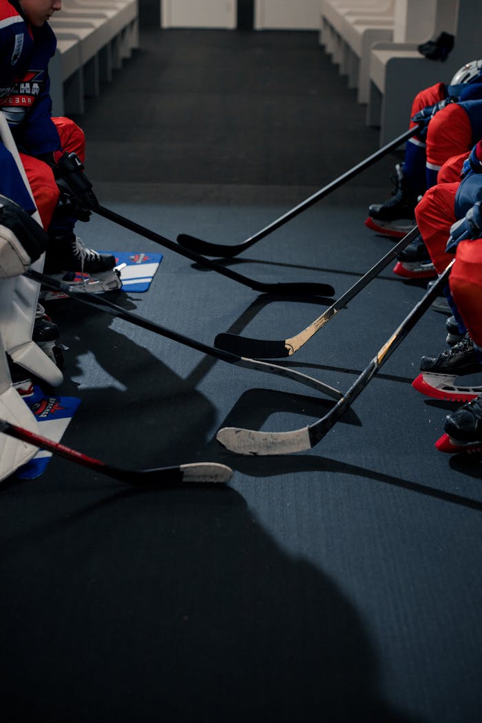 Hockey players' sticks aligned on the floor in a locker room setting, showcasing team readiness.